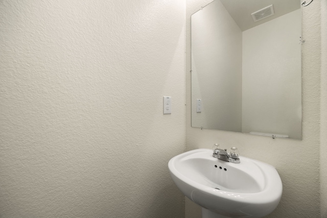 bathroom with a textured wall, a sink, and visible vents