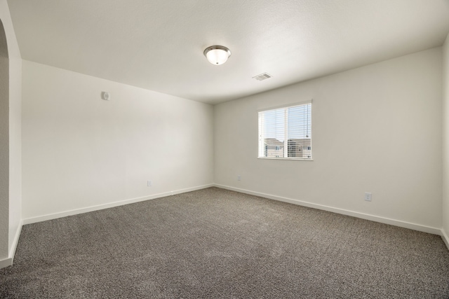 spare room with dark carpet, visible vents, and baseboards