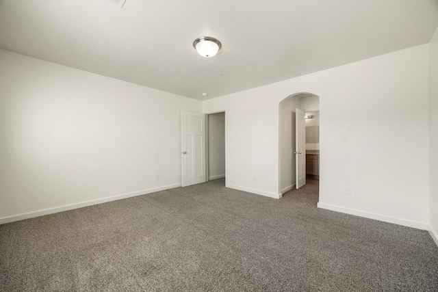 empty room with arched walkways, dark carpet, and baseboards