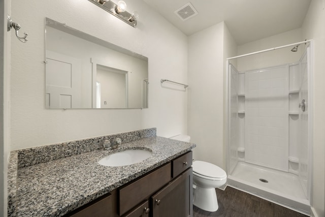 full bathroom featuring visible vents, tiled shower, toilet, wood finished floors, and vanity