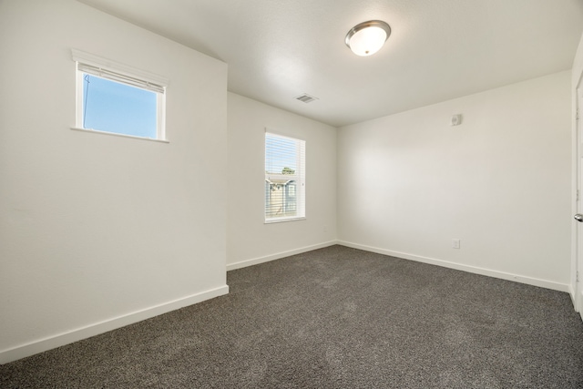 spare room featuring dark colored carpet, visible vents, and baseboards