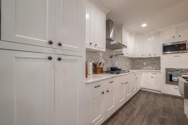 kitchen with dark wood-style flooring, tasteful backsplash, appliances with stainless steel finishes, white cabinets, and wall chimney exhaust hood