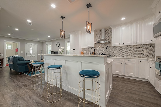 kitchen featuring dark wood finished floors, tasteful backsplash, a kitchen bar, white cabinetry, and wall chimney exhaust hood