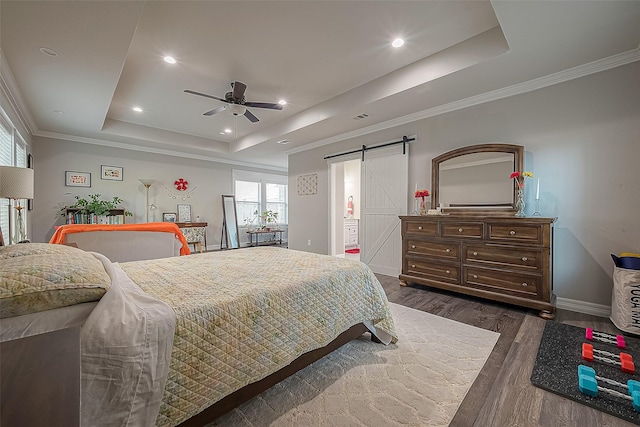 bedroom with dark wood-style floors, a tray ceiling, a barn door, and crown molding