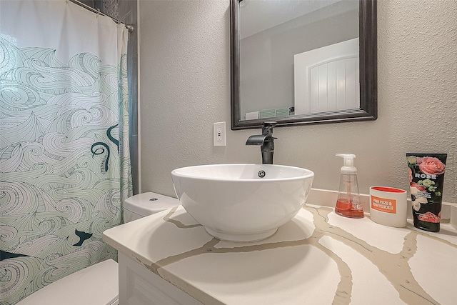 bathroom featuring a textured wall, vanity, toilet, and a shower with curtain