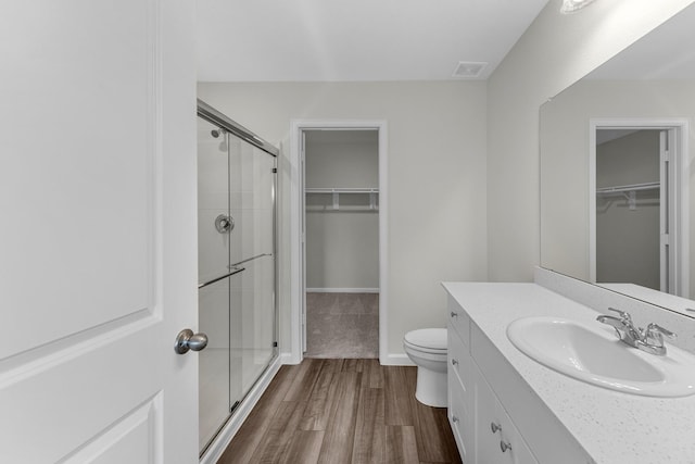 bathroom featuring visible vents, toilet, wood finished floors, a walk in closet, and a shower stall