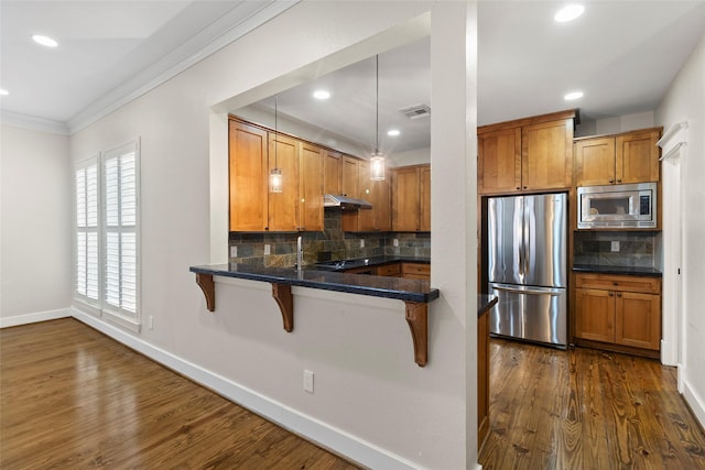 kitchen featuring dark wood-style flooring, a breakfast bar area, stainless steel appliances, brown cabinetry, and under cabinet range hood