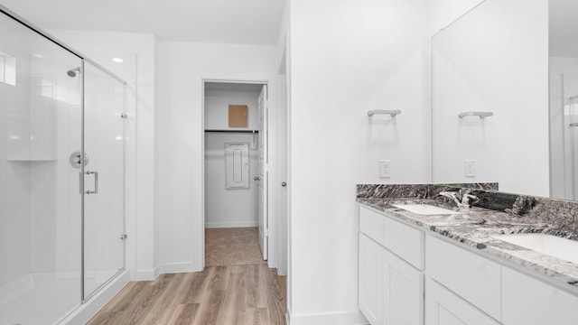 full bathroom featuring double vanity, a stall shower, a sink, and wood finished floors