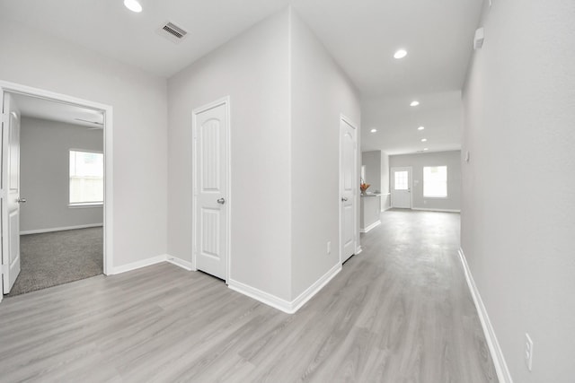 hallway featuring baseboards, light wood-style flooring, visible vents, and a wealth of natural light