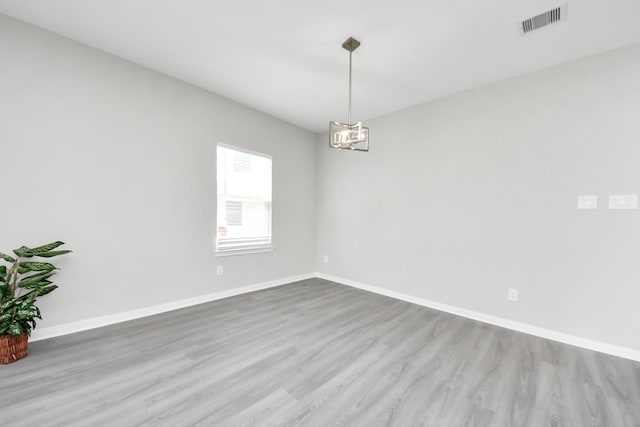 spare room with an inviting chandelier, visible vents, baseboards, and wood finished floors