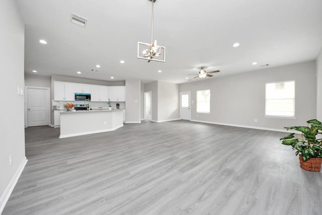 unfurnished living room with recessed lighting, visible vents, light wood-style flooring, baseboards, and ceiling fan with notable chandelier