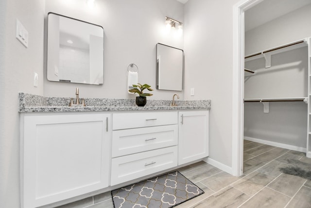 bathroom with double vanity, wood finish floors, a sink, and baseboards