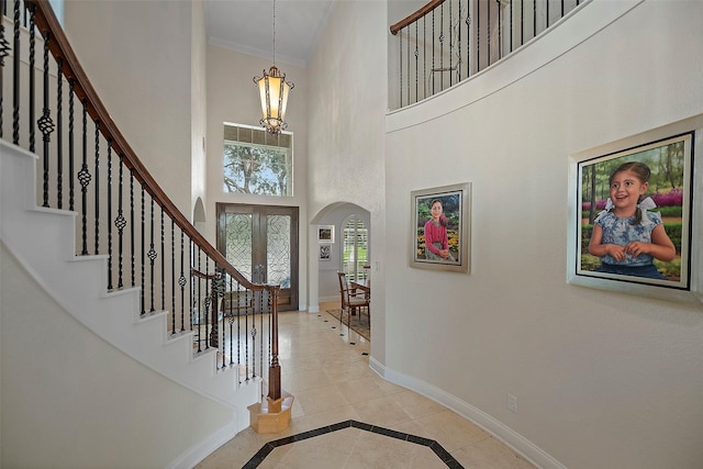 foyer entrance with baseboards, arched walkways, ornamental molding, a high ceiling, and stairs