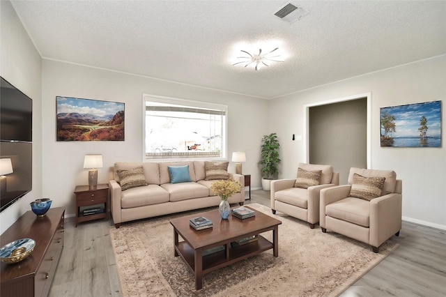 living room featuring a textured ceiling, baseboards, visible vents, and light wood-style floors