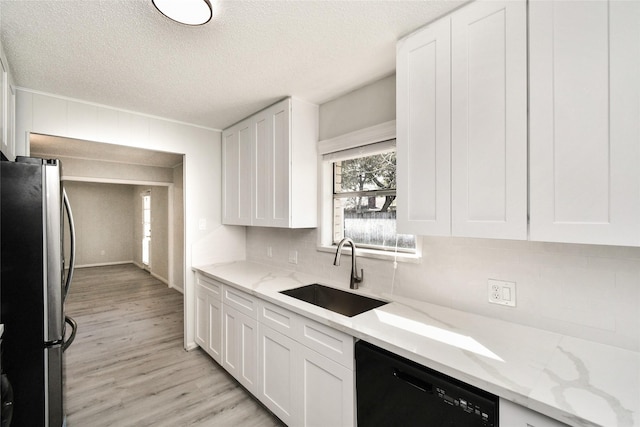 kitchen featuring black dishwasher, white cabinetry, a sink, and freestanding refrigerator