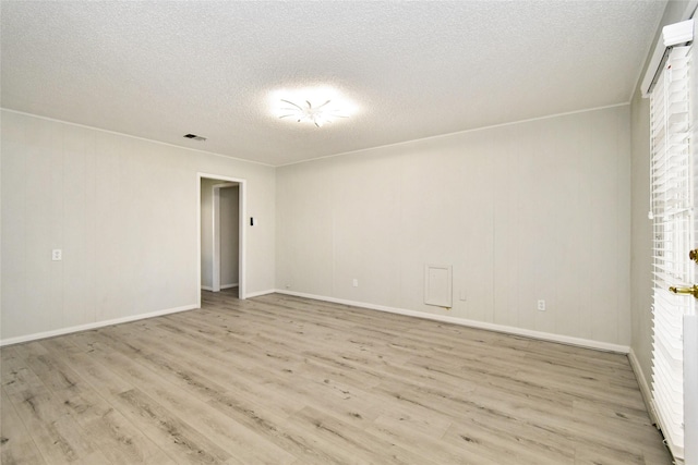 empty room featuring a textured ceiling, light wood-type flooring, visible vents, and baseboards