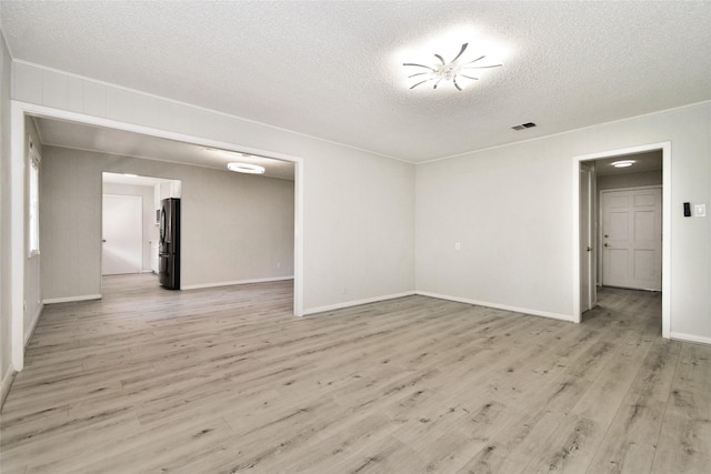 spare room featuring light wood-type flooring, baseboards, and a textured ceiling