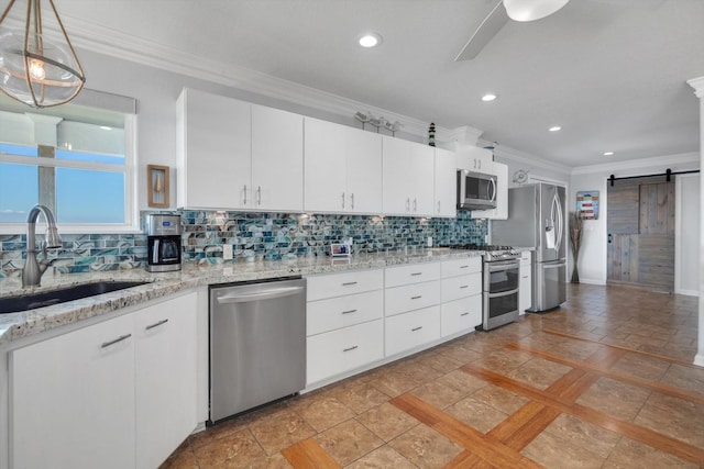 kitchen featuring a barn door, a sink, ornamental molding, appliances with stainless steel finishes, and decorative backsplash