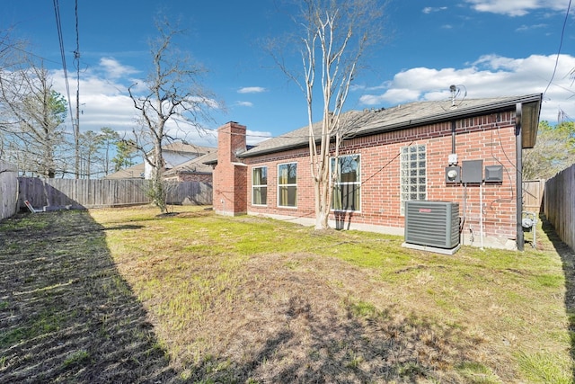 back of house featuring a fenced backyard, central AC, brick siding, a lawn, and a chimney