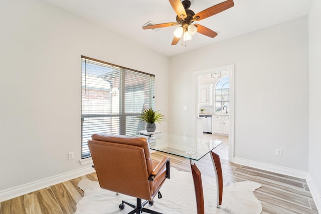 office area with ceiling fan, light wood finished floors, a sink, and baseboards