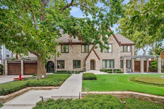 tudor-style house with a front yard, concrete driveway, and a pergola