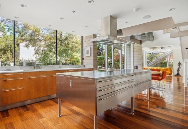 kitchen featuring light wood finished floors, island range hood, brown cabinetry, light countertops, and a sink