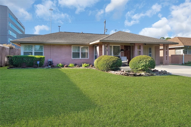 ranch-style house with brick siding, a shingled roof, concrete driveway, fence, and a front lawn