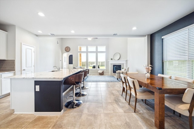 kitchen featuring light stone counters, a tiled fireplace, a kitchen island with sink, white cabinets, and a sink