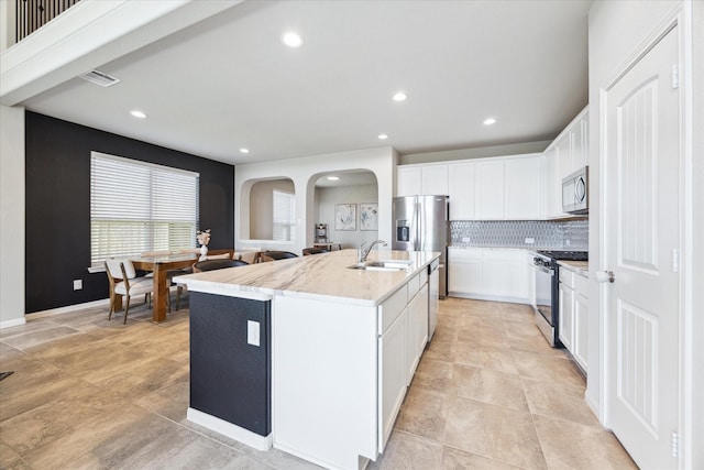 kitchen with stainless steel appliances, a sink, visible vents, backsplash, and an island with sink