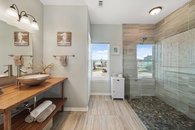 full bath featuring a sink, a tile shower, visible vents, and baseboards