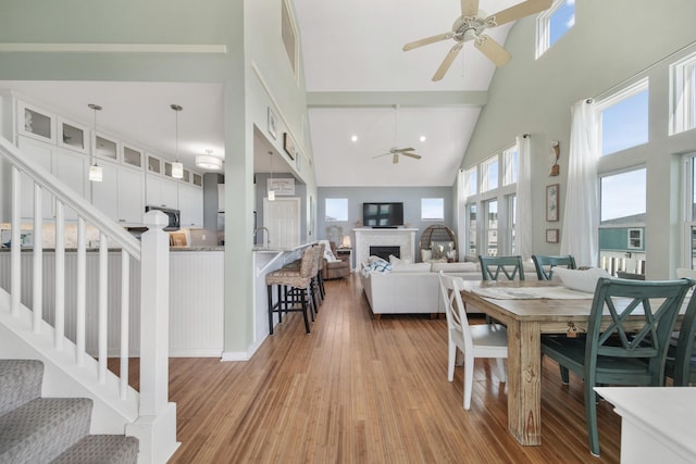 dining area with ceiling fan, stairway, a high ceiling, light wood-type flooring, and a fireplace