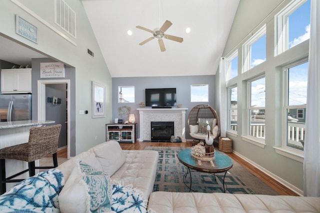 living area featuring high vaulted ceiling, a fireplace, visible vents, and wood finished floors