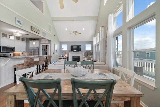 dining room with a fireplace, light wood finished floors, visible vents, ceiling fan, and high vaulted ceiling