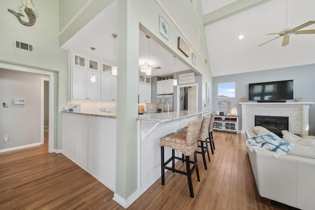 kitchen featuring glass insert cabinets, light wood-type flooring, visible vents, and high vaulted ceiling