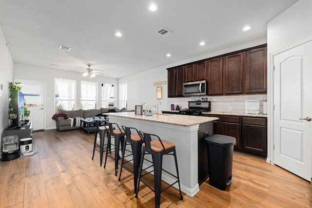 kitchen with light wood finished floors, tasteful backsplash, a center island with sink, appliances with stainless steel finishes, and a kitchen bar