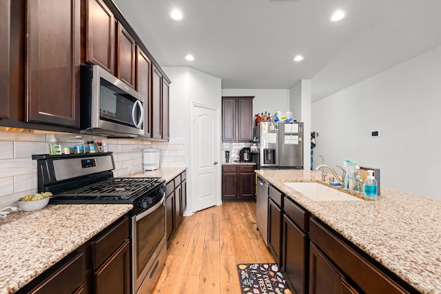 kitchen with stainless steel appliances, backsplash, light wood-style flooring, a sink, and dark brown cabinetry