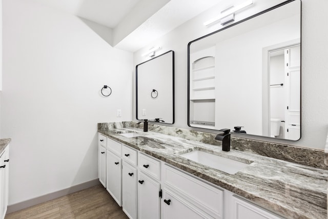 full bath with wood finished floors, a sink, baseboards, and double vanity