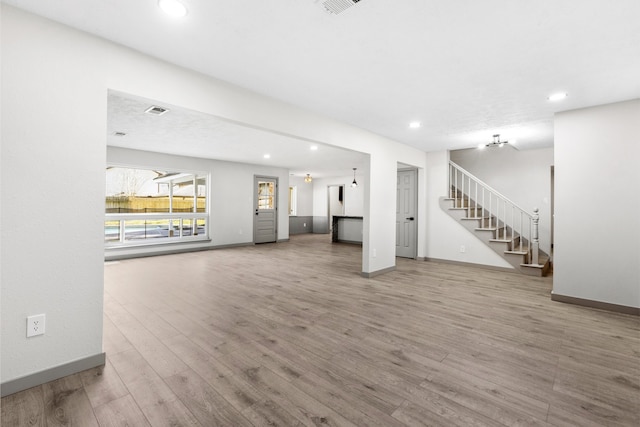 unfurnished living room with stairway, baseboards, and wood finished floors