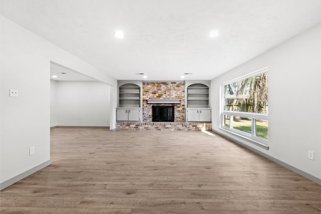 unfurnished living room with a brick fireplace, built in shelves, baseboards, and wood finished floors