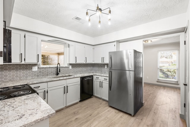 kitchen featuring black dishwasher, decorative backsplash, light wood-style floors, freestanding refrigerator, and a sink