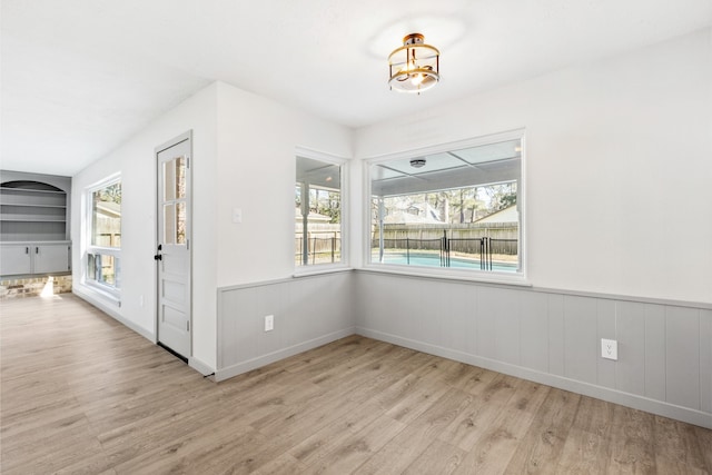 unfurnished dining area with a wainscoted wall, built in features, and wood finished floors