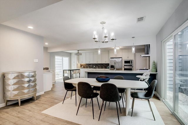 dining space with baseboards, light wood-style flooring, visible vents, and a notable chandelier