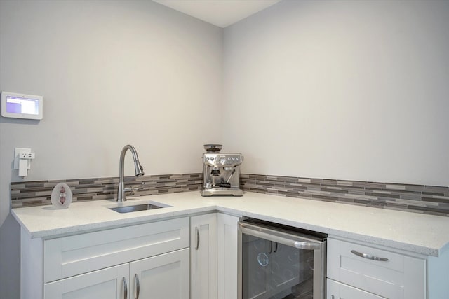 kitchen with beverage cooler, a sink, white cabinets, decorative backsplash, and light stone countertops