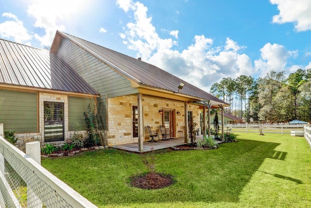 rear view of property with stone siding, a fenced backyard, metal roof, a yard, and a patio area