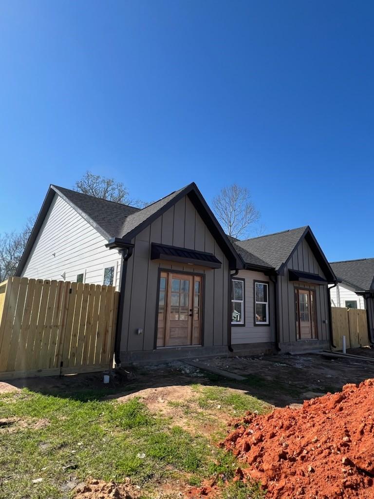 back of property with board and batten siding, roof with shingles, and fence