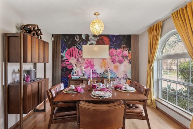 dining space with a chandelier, an accent wall, light wood finished floors, and wallpapered walls