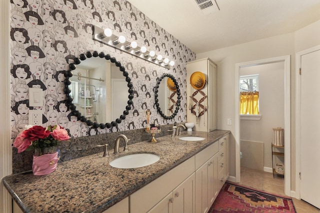 full bath with double vanity, visible vents, a sink, and wallpapered walls