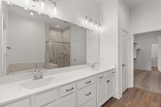 bathroom with double vanity, wood finished floors, a sink, and a marble finish shower