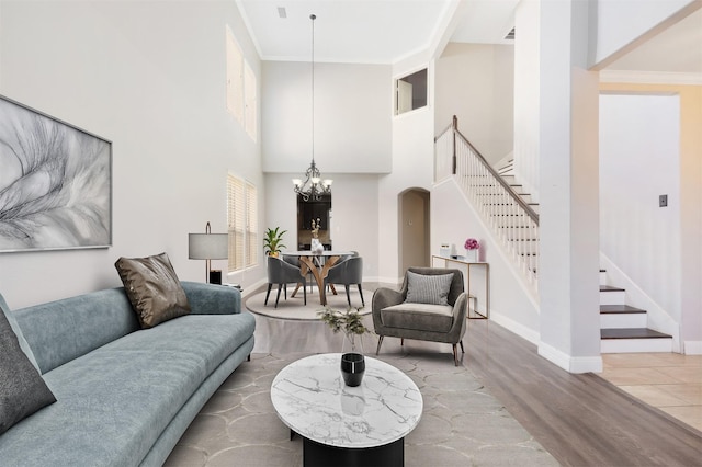 living room with an inviting chandelier, ornamental molding, wood finished floors, baseboards, and stairs