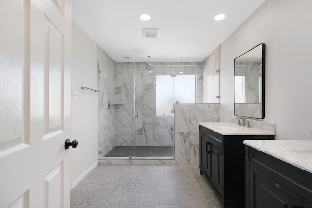 full bath featuring a marble finish shower, visible vents, a sink, two vanities, and recessed lighting